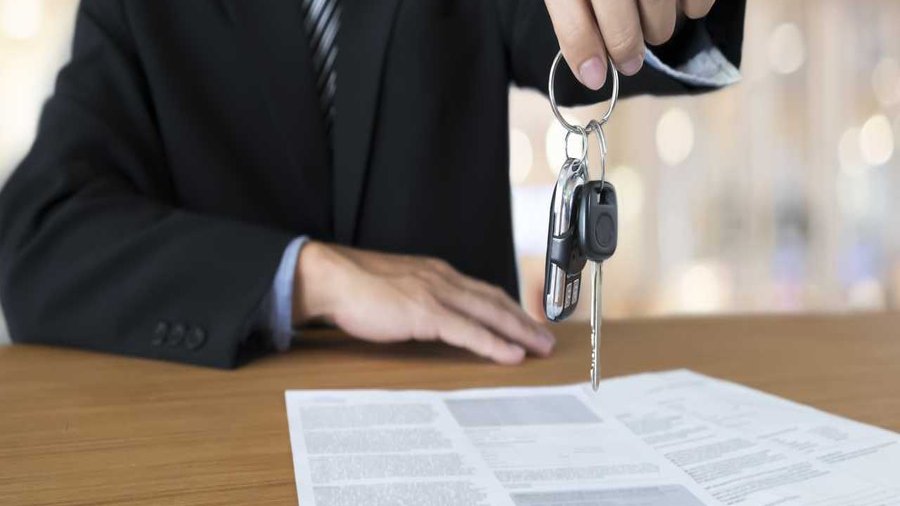 Car dealer handing over keys with finance documents on desk